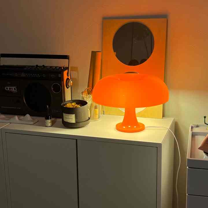 ホワイトトーンのキッチン脇のサイドボード、オレンジのテーブルランプと丸い鏡が配置されたシンプルで雰囲気のあるインテリア