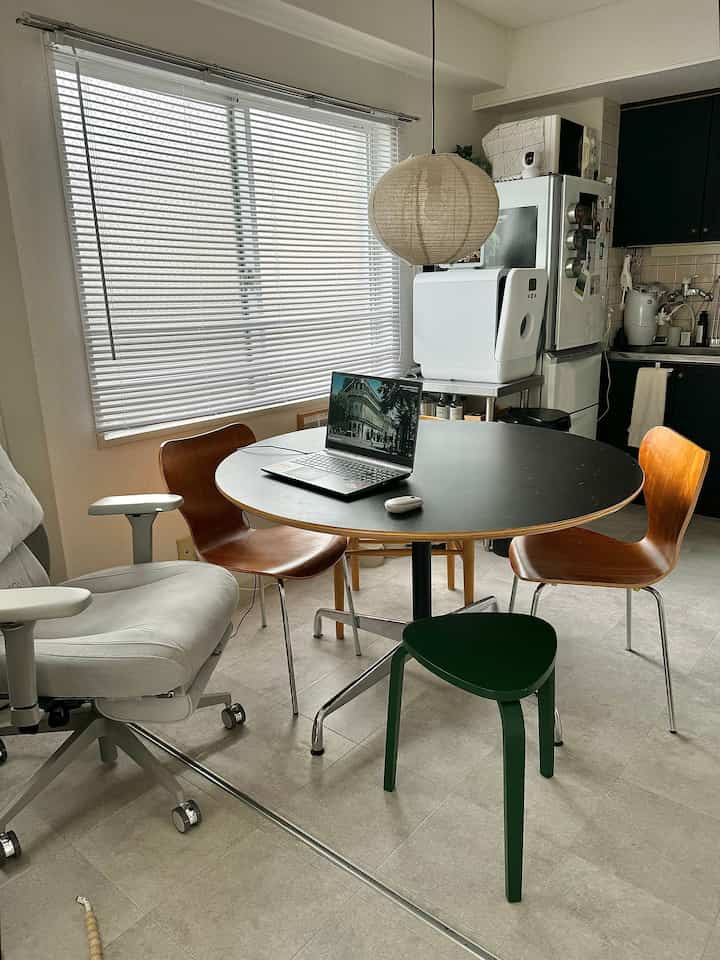 Natural-toned dining room featuring a round dining table, wooden chairs, and a green stool in a simple, cozy space