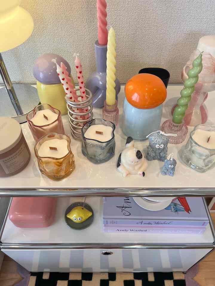 A cozy living room with white and pink tones featuring a cabinet topped with various uniquely shaped and colored candles