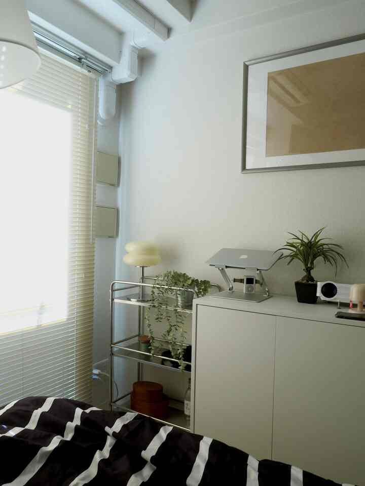 ホワイトトーンのワンルーム寝室、ブラインドとベッド、シルバー家具が配置されたシンプルなインテリア