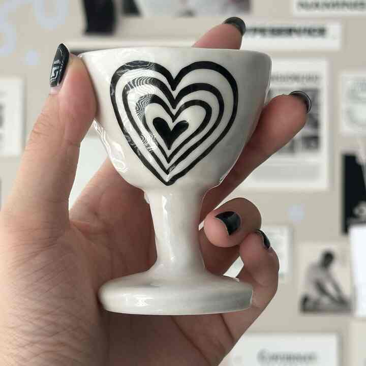 Image of a white heart-shaped ceramic bowl with black heart patterns held in hand against a blurred background