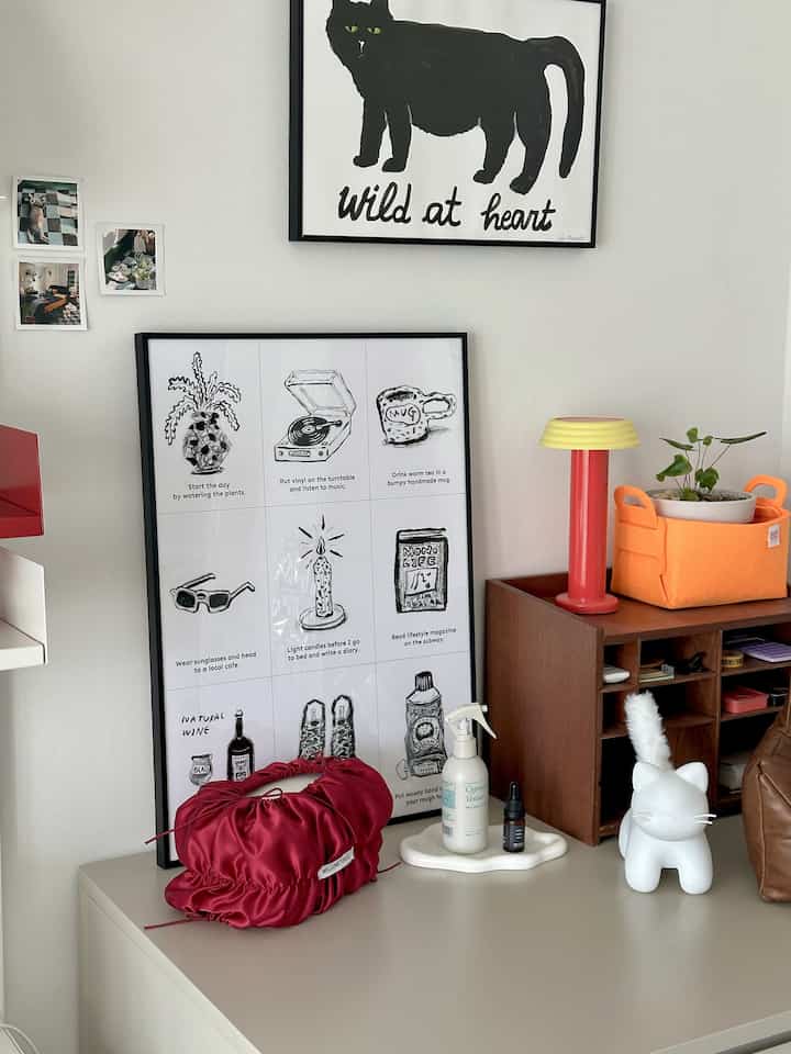 ナチュラルトーンの書斎、猫型のムードランプと赤いバッグ、レトロなポスターが配置された雰囲気のあるインテリア