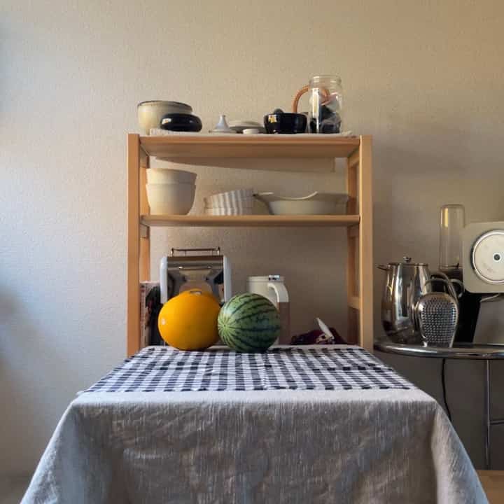 ナチュラルカラーのキッチン、パイン棚と折りたたみテーブルの上に黄色いメロンとスイカが置かれた雰囲気のある空間