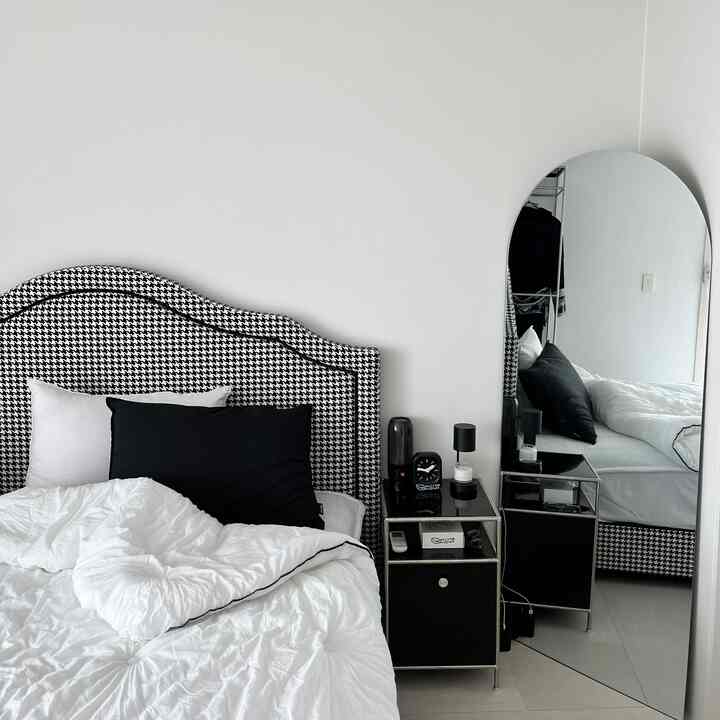 Monotone black and white bedroom featuring a clean checkered headboard, nightstand, and arched full-length mirror in a simple setting