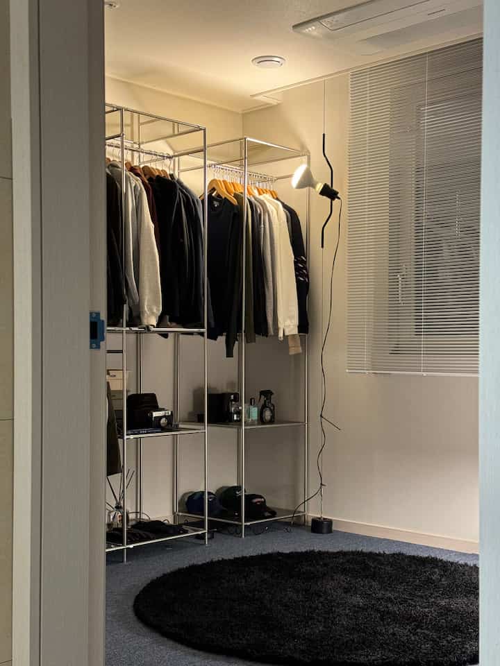 Mid-century modern walk-in closet with stainless steel clothes racks, black round rug and calm blue carpet flooring