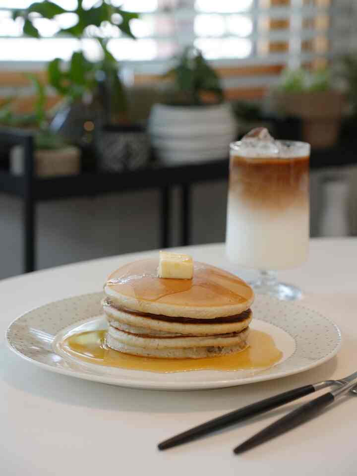 白を基調とした丸テーブルの上にシロップとバターをのせたパンケーキとアイスコーヒーが置かれた雰囲気のあるカフェ風空間