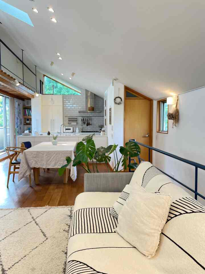 白と木目調が調和したナチュラルなリビング、ソファとダイニングテーブルが配置された抜け感のある空間。