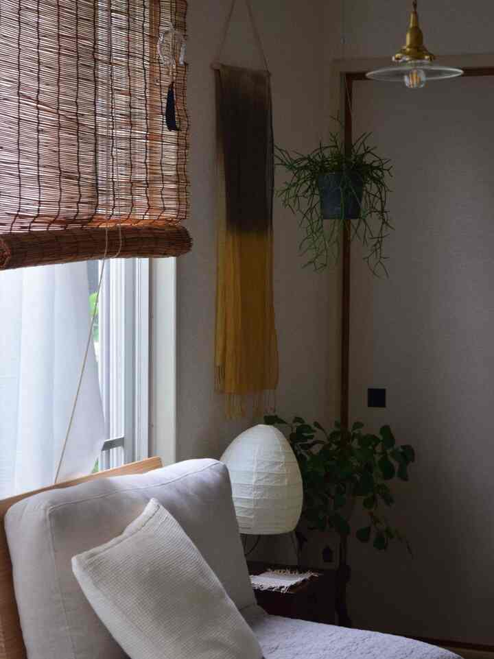 ナチュラルな色調のリビング、ベージュのソファと竹のすだれ、白いランプと植物が調和した温かみのあるインテリア