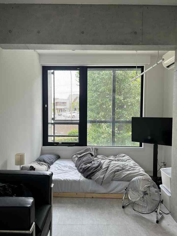 白とグレーのトーンのワンルーム寝室、ブラックのソファとメタルファンが配置されたモダンなインテリア