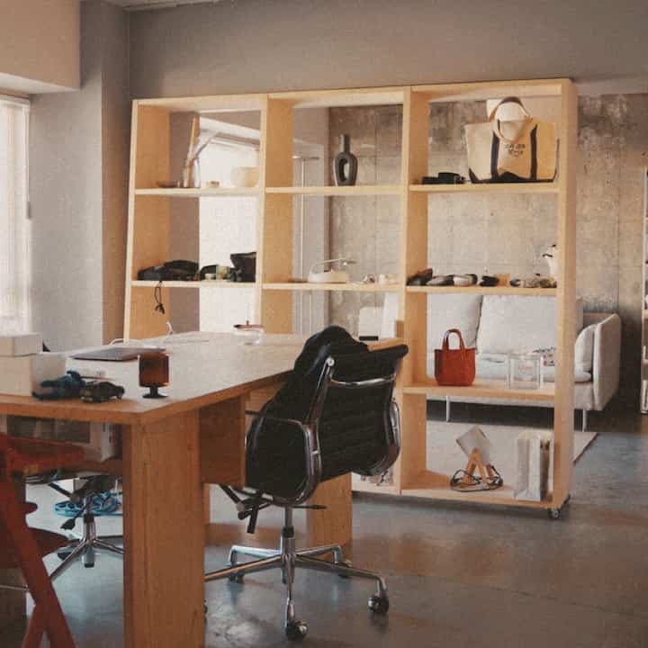 ナチュラルトーンのリビング兼ホームオフィス、木目調の家具とオープンシェルフが配置された印象的な空間