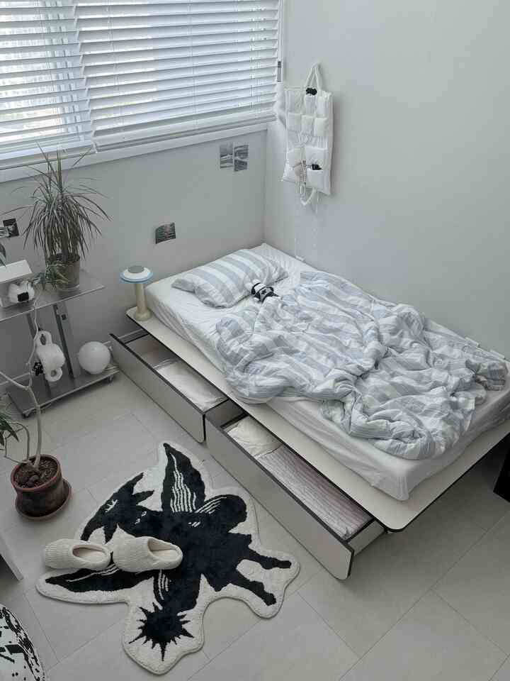 ホワイトとブルーのワンルーム寝室、収納型ロータイプベッドと植物が配置された清潔で居心地の良いインテリア