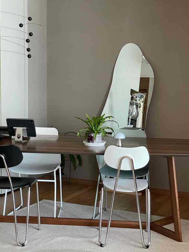 Modern dining room with beige walls, wood tone dining table, and various colored dining chairs arranged