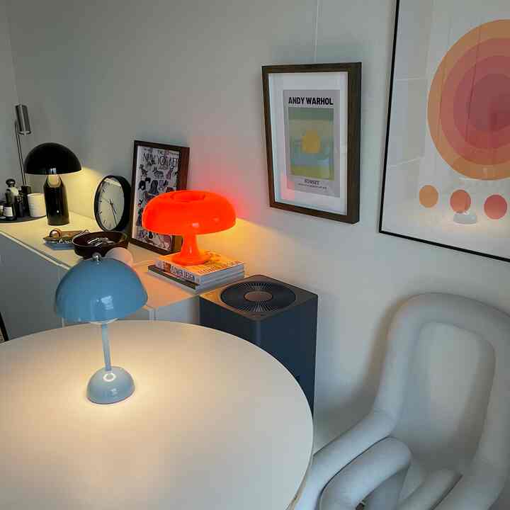 白を基調としたナチュラルなリビング、丸テーブルと個性的な椅子、ポスターと複数の照明が配置された印象的な空間