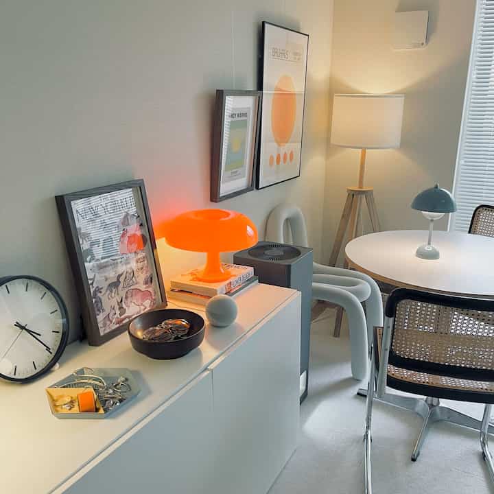 白と木目調が調和したモダンなダイニングルーム、オレンジのテーブルランプと額縁が温かみのある雰囲気を演出