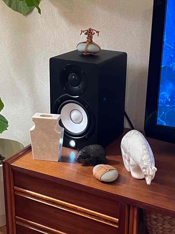 暖かみのあるブラウンの木目調家具の上に黒いスタジオモニターと様々なオブジェが配置されたリビングスペース