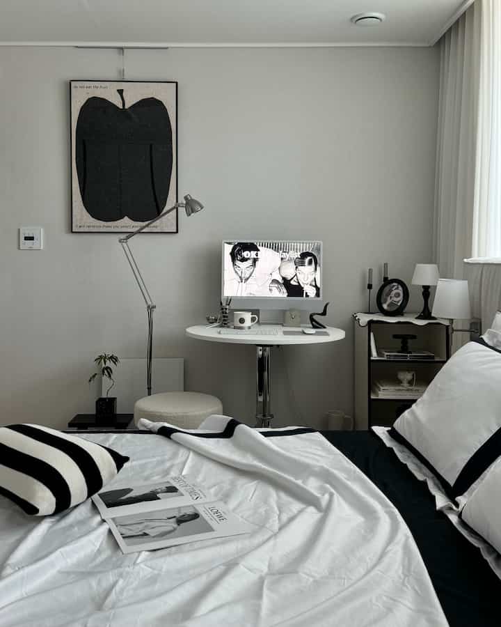 Black and white toned bedroom and study space with round table and iMac, featuring simple and modern interior design