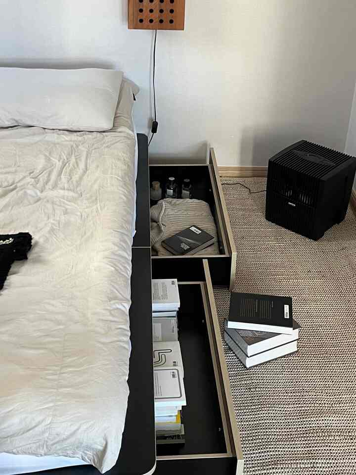 ホワイトとブラックのトーンの寝室、収納付きベッドフレームとラタンラグが配置された落ち着いた空間