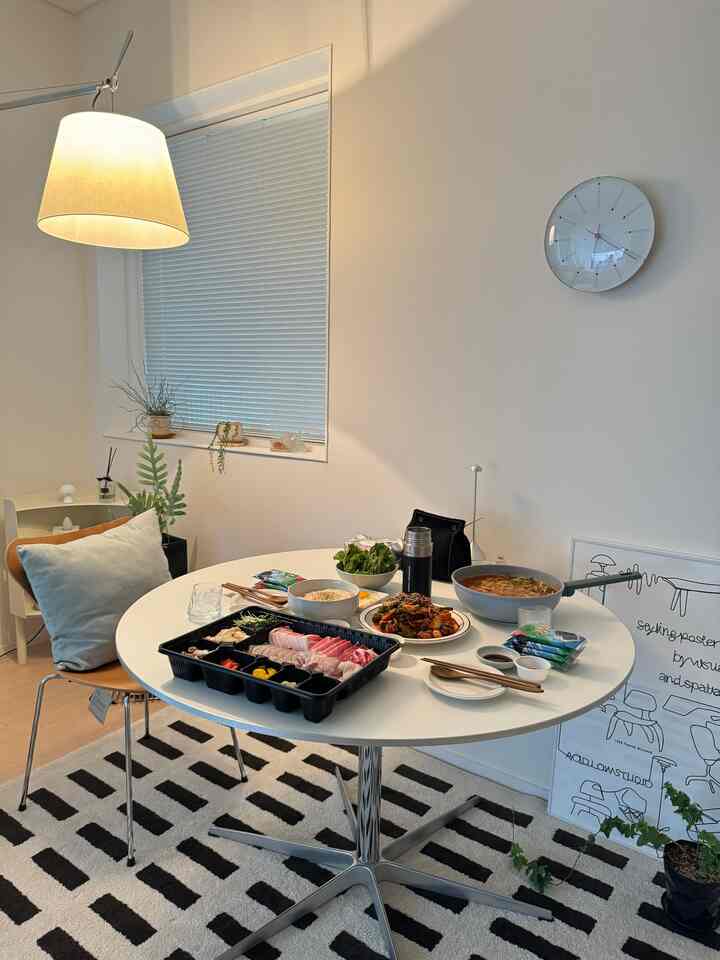 White and black toned dining room featuring round table, chairs, pendant light, and poster creating a clean modern space