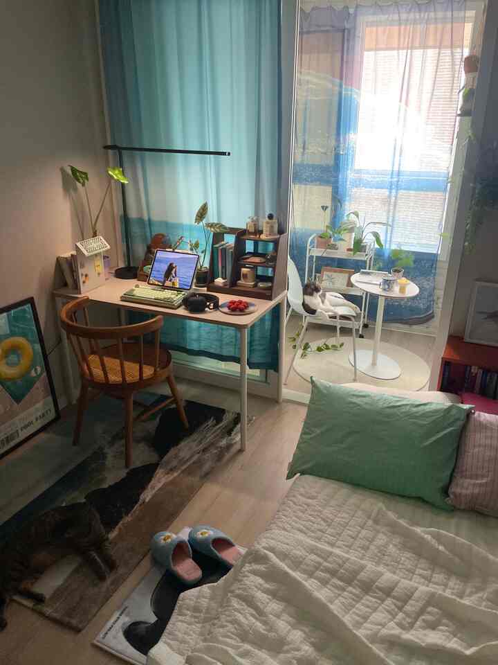 ブルーのカーテンが印象的な寝室、木製の椅子と机の上にタブレットと植物が配置された雰囲気ある空間