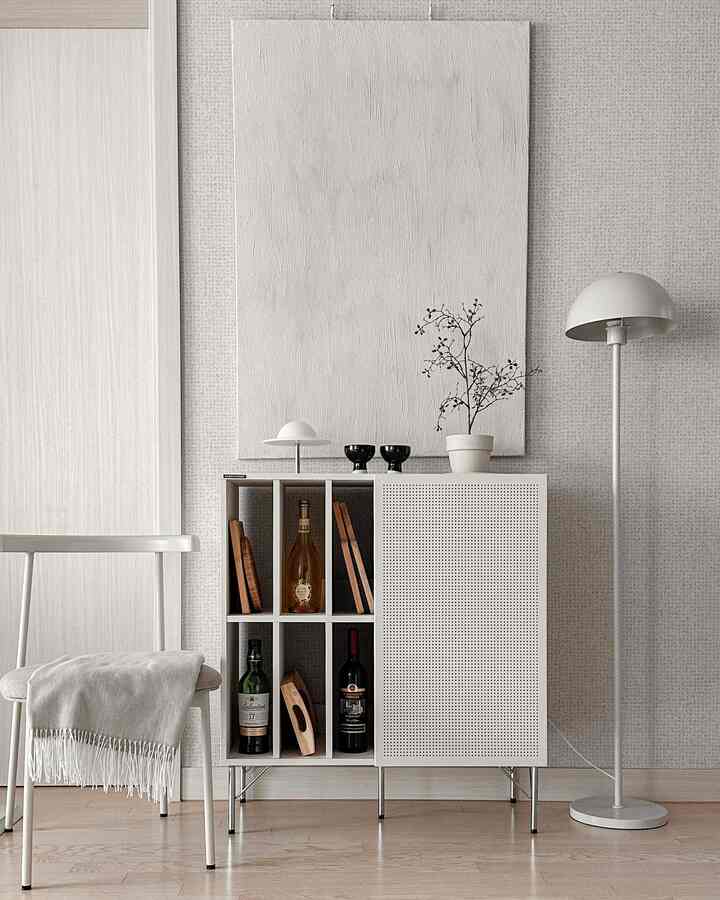 A bright white and natural wood toned living room featuring an archive storage cabinet, simple floor lamp, and a minimalist chair