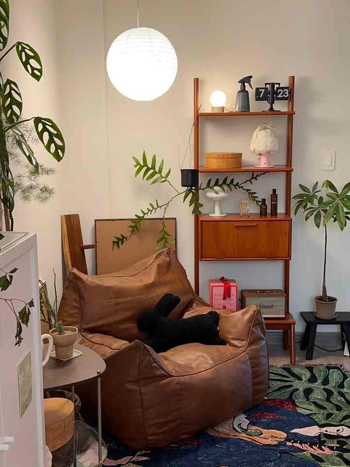 Cozy loft room with white walls and wood tone shelves, featuring a brown bean bag sofa and multiple plants in a relaxing space