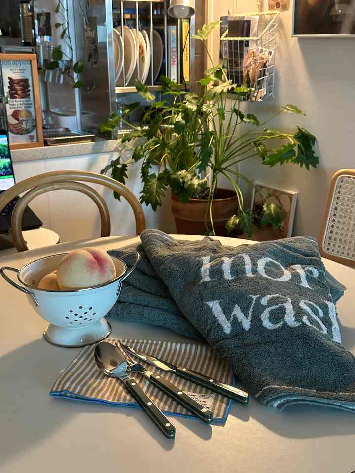 白いテーブルの上にグリーンのタオルとカトラリー、白のコランダーが置かれたナチュラルでモダンなキッチンインテリア