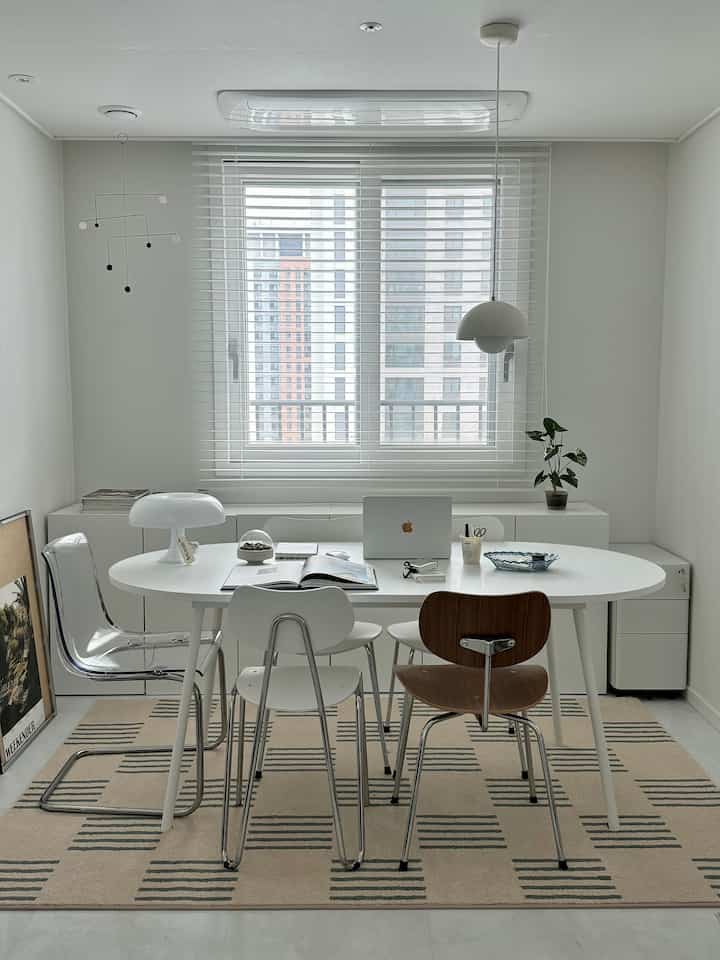白を基調としたダイニング兼書斎、白い楕円形のテーブルとさまざまな素材の椅子が配置された清潔感のある空間