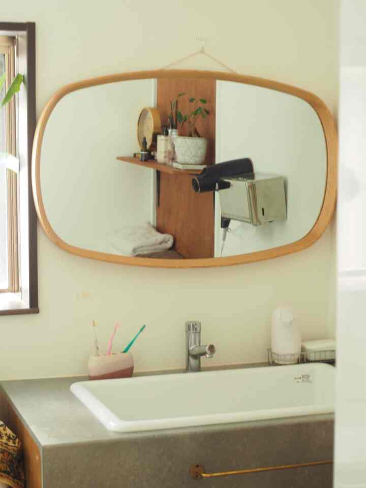 White-walled bathroom space featuring a wood-toned oval mirror above the washbasin with natural decor