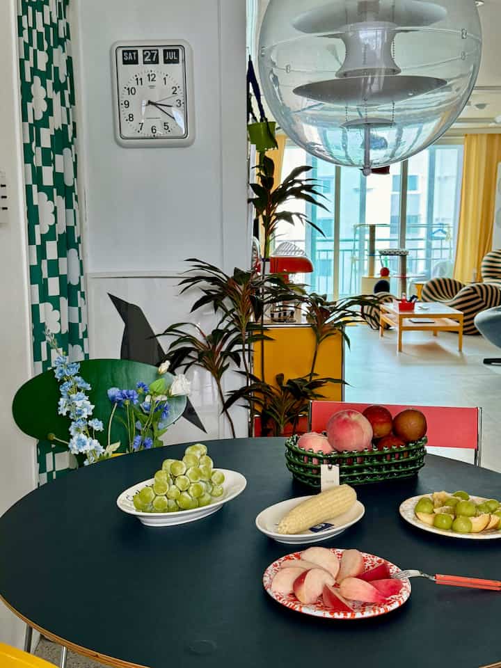 Green and black toned kitchen and dining room featuring a round dining table with fruit and plates centrally placed in a modern setting