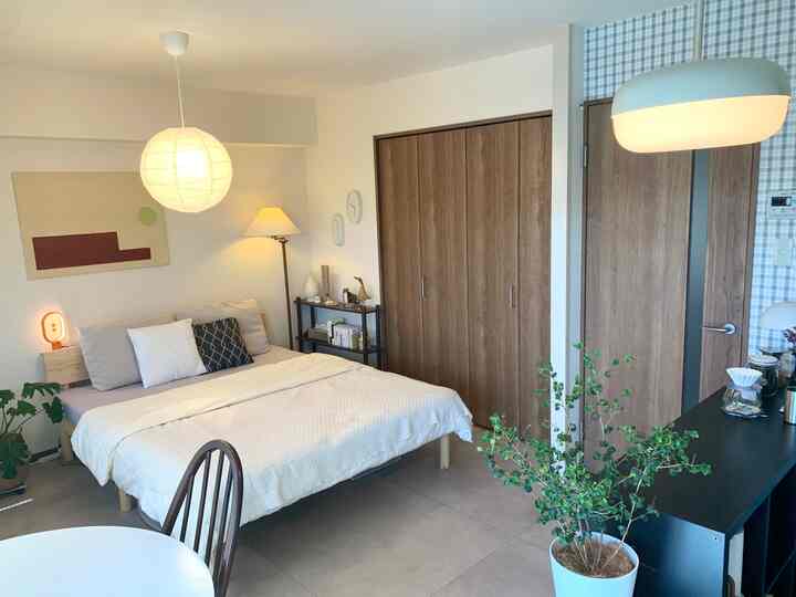 ホワイトとベージュのトーンの13畳1LDK、クイーンベッドと木目調のクローゼットが配置されたホテルライクな空間