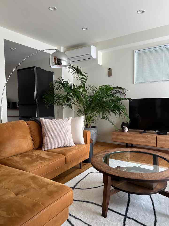 暖かみのあるブラウンとナチュラルカラーのリビング、大型ソファと円形のコーヒーテーブル、テレビ台が調和した居心地の良い空間