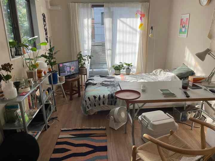 Natural wood tone and white curtains in a cozy 1K bedroom featuring multiple plants and functional furniture