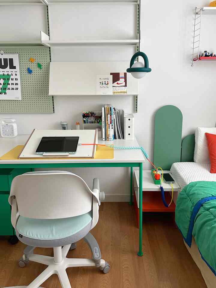 Bright bedroom and home office space featuring white and green tones with a desk and office chair neatly arranged