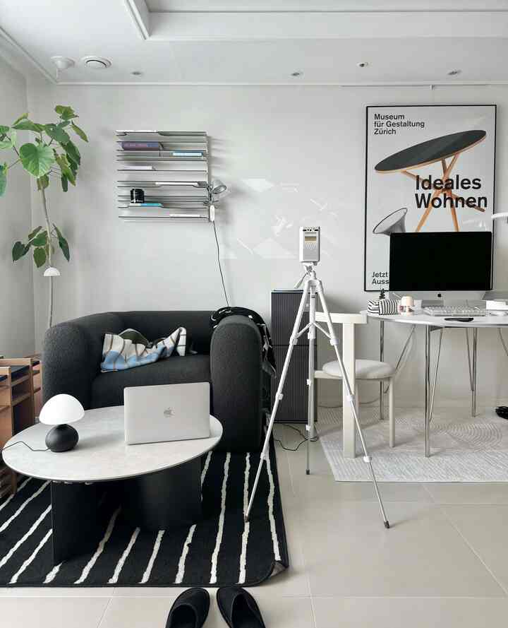 Modern living room and home office in white tones featuring a black armchair, desk, and indoor plant with clean design