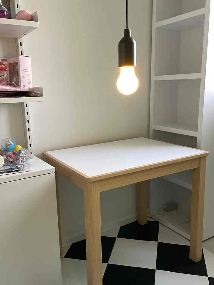 白と木目調が調和する小さな部屋のコーナー、チェッカーボードの床タイルとシンプルなテーブル、照明が配置されたミニマルな空間