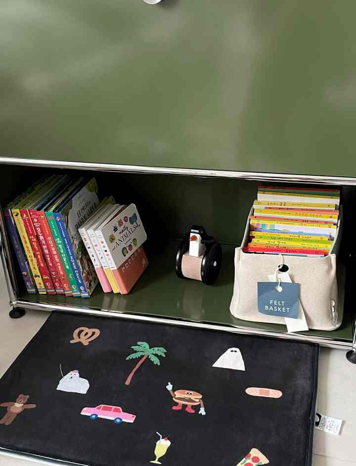 Children's storage space featuring black mat and green furniture with books and toys