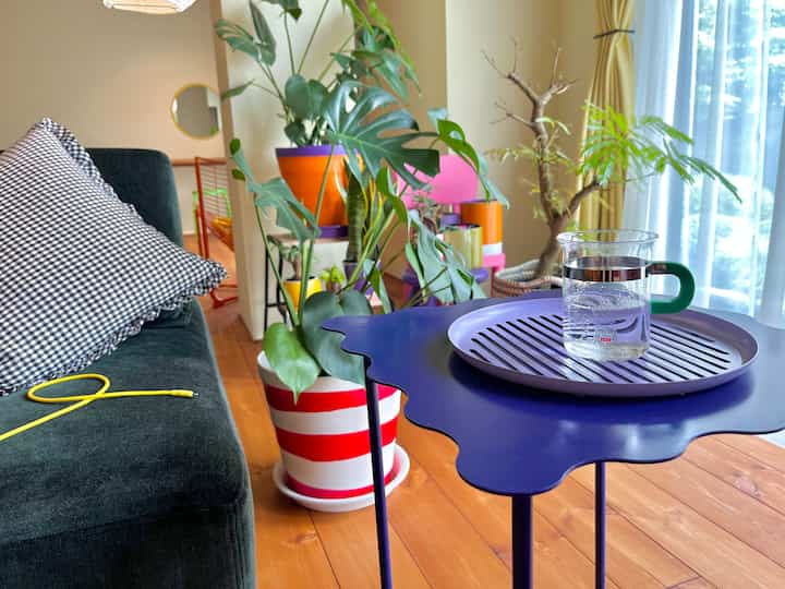 ナチュラルな木目調と緑の植物が配置されたリビング、青いテーブルにトレイとグラスが置かれた明るく居心地の良い空間
