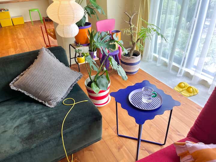 木目調のリビングルーム、白い和紙の照明とカラフルな椅子、豊かな観葉植物が配置された印象的な空間