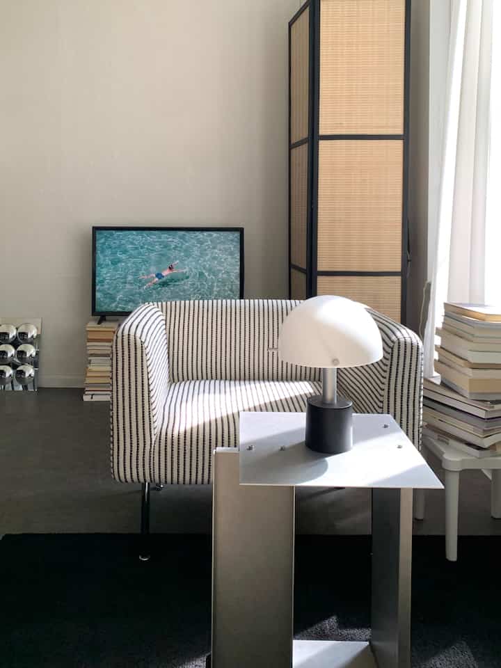 Bright living room with natural light featuring a white and black striped armchair, modern metal side table with lamp, and framed artwork