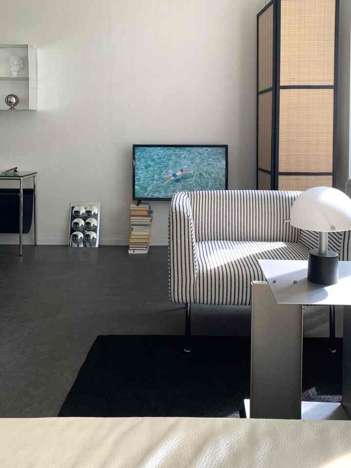 白と黒のトーンのリビング、ストライプのソファとメタルのサイドテーブル、テレビが配置されたモダンでミニマルな空間