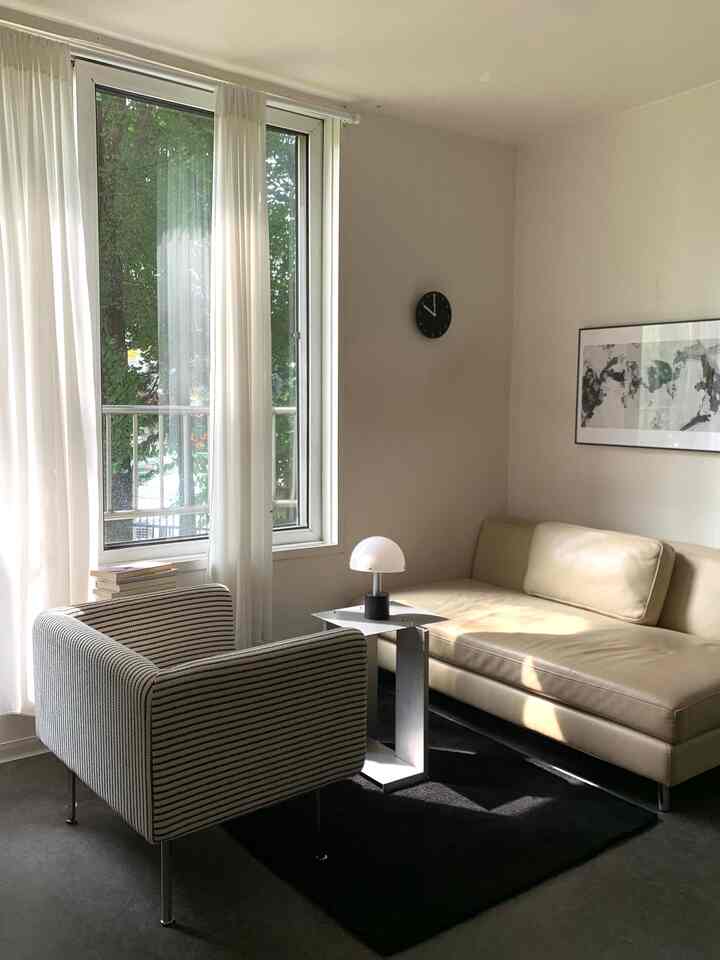 Bright white-toned living room featuring a beige sofa and striped armchair in a modern cozy setting
