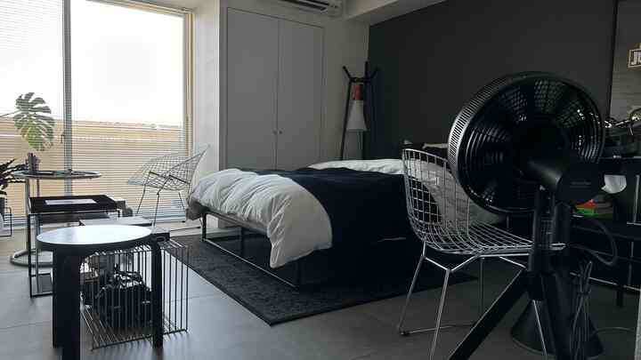Black and white toned bedroom featuring modern wire furniture and a fan, with a clean minimalist atmosphere