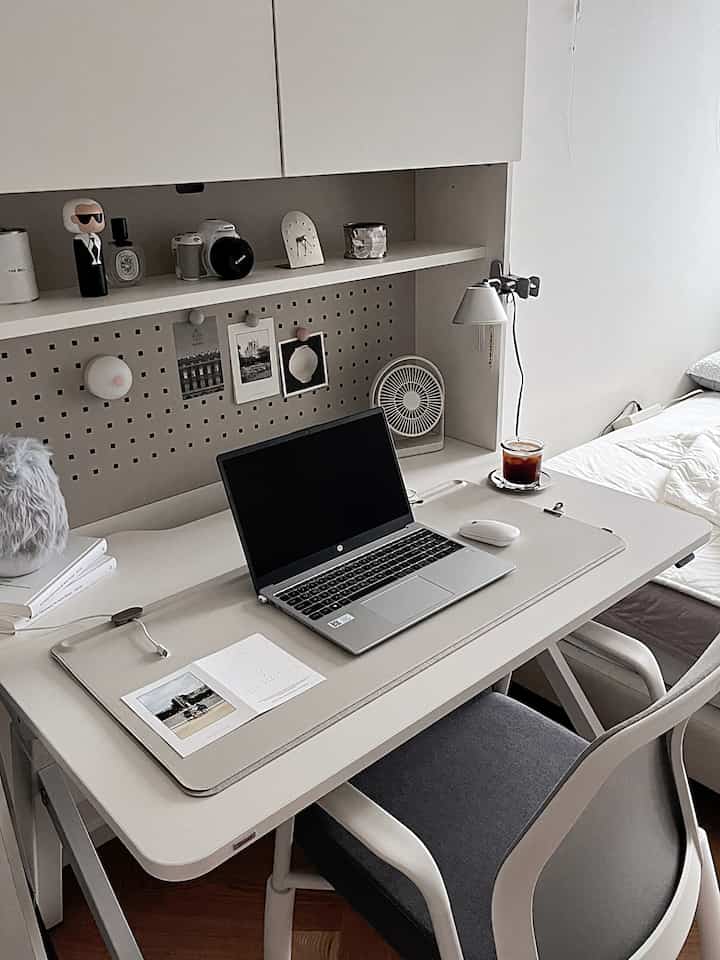 White-toned home office space featuring a desk with a laptop and organized shelves, creating a simple working area