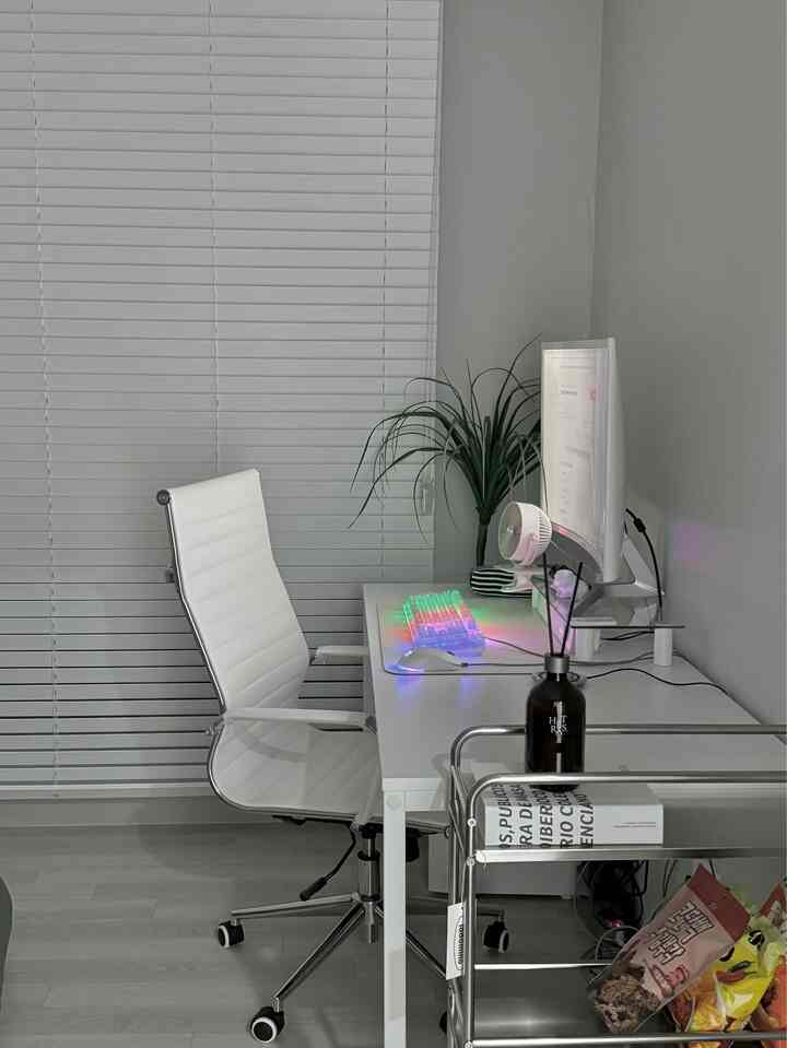 A modern white-toned home office featuring a desk with an RGB keyboard and an ergonomic office chair, creating a clean workspace