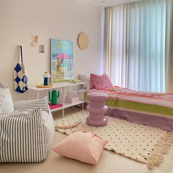 A cozy single bedroom with dominant white and pink tones, featuring a bean bag sofa and a rug creating a comfortable atmosphere