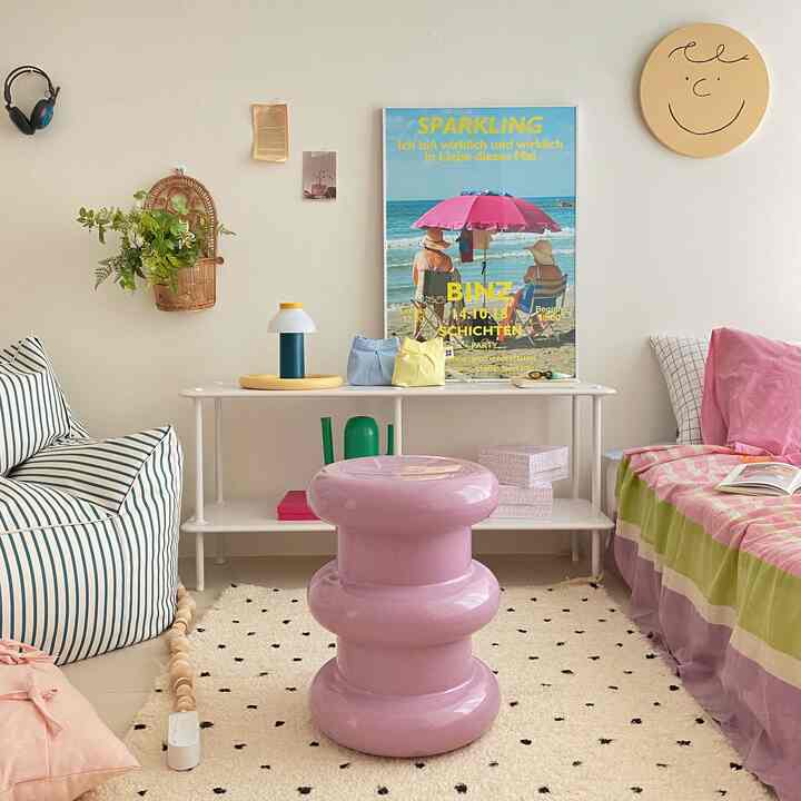 Ivory-toned Nordic living room featuring a pink sculptural stool, striped sofa, and bright beach poster with cozy atmosphere