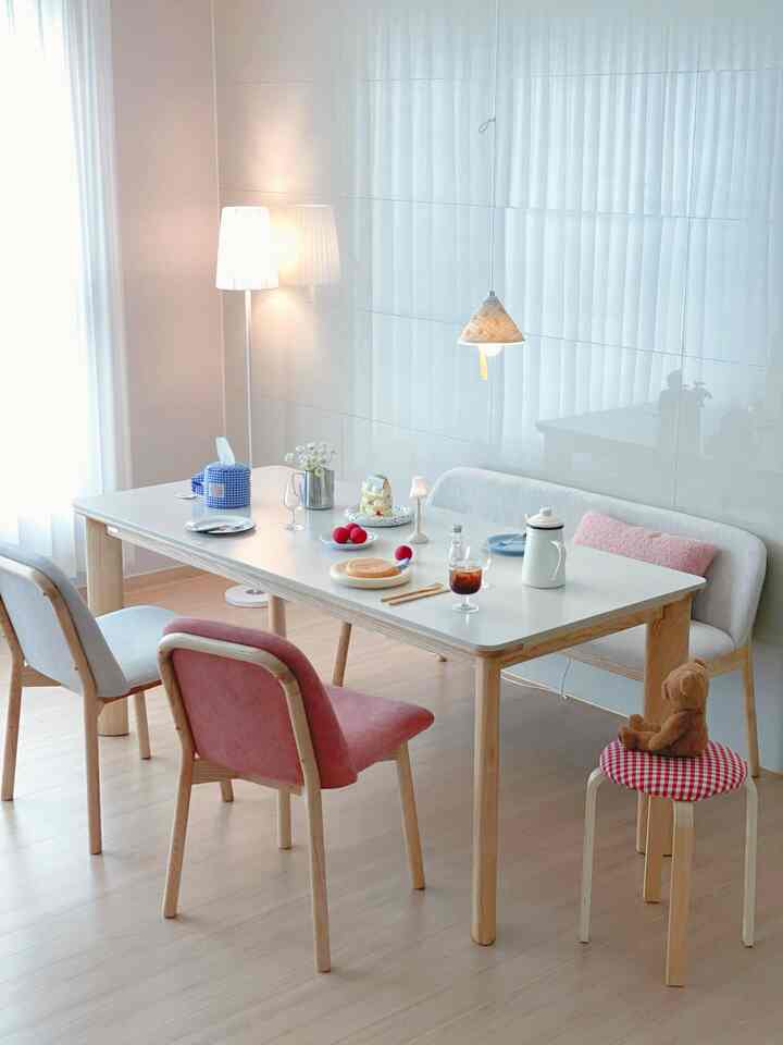白とナチュラルウッド調のリビング、セラミックのダイニングテーブルとピンクの椅子、かわいいクマのぬいぐるみがある雰囲気の良いブランチ空間