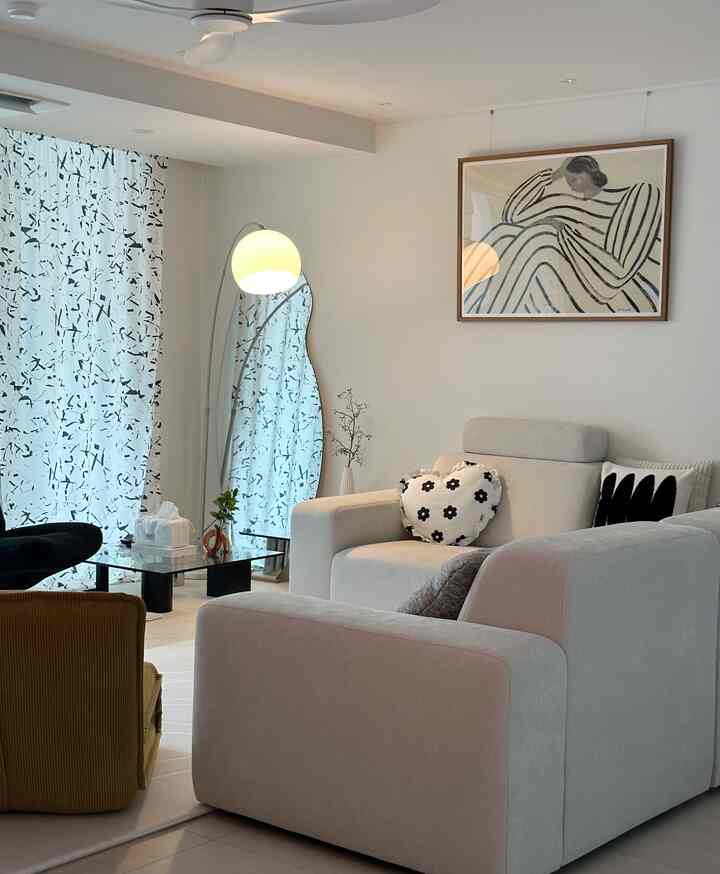 A white-toned living room featuring a cream sectional sofa and uniquely shaped coffee table arranged for a cozy atmosphere