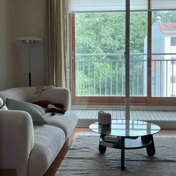 ナチュラルなブラウンとホワイトの色調のリビング、ソファと丸いガラスのコーヒーテーブルが配置された落ち着いた空間