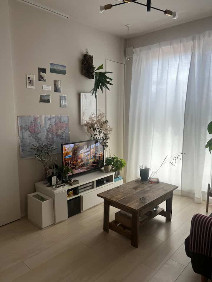 ナチュラルな木目調とホワイトの北欧風リビング、中央に木製のローテーブルとテレビ台、壁にポスターと観葉植物が配置されたシンプルな雰囲気のインテリア